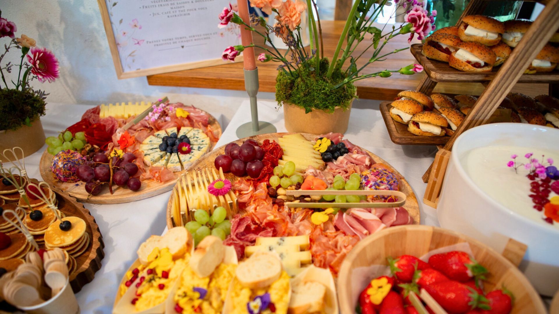 Un assortiment de planches de charcuterie avec fruits, fromages, viandes et petits desserts lors d'un événement traiteur avec décoration florale.
