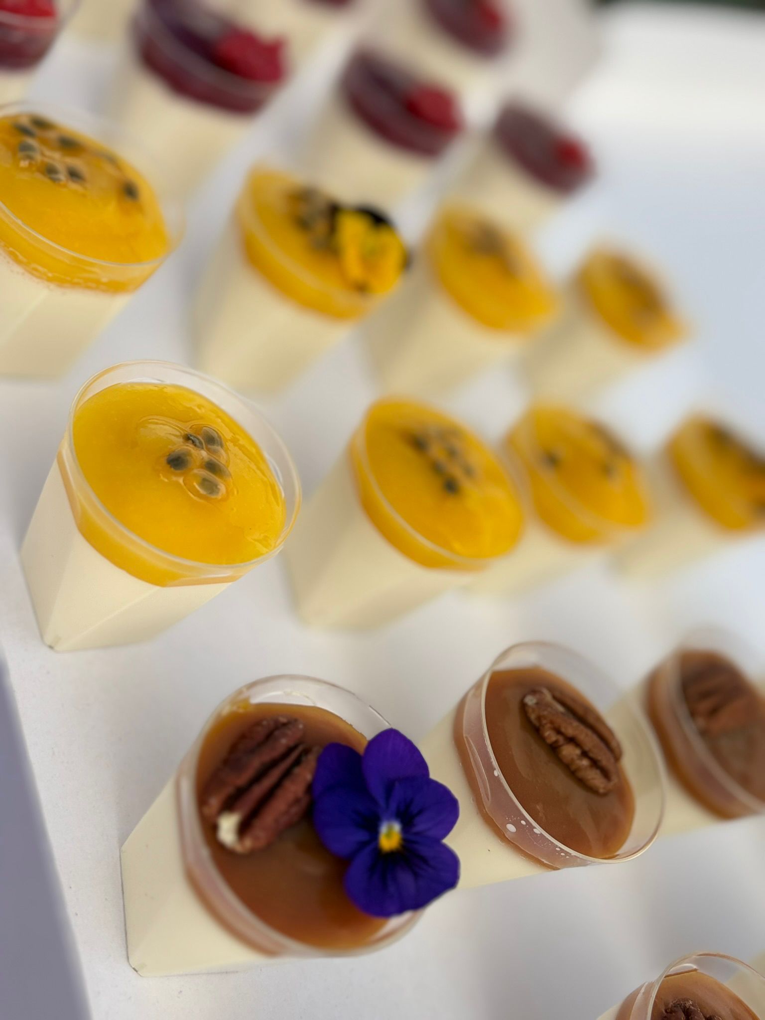 Une personne vêtue de noir prépare un élégant buffet d'amuse-gueules composé de brochettes et de petites bouchées présentées sur des présentoirs en verre à étages.