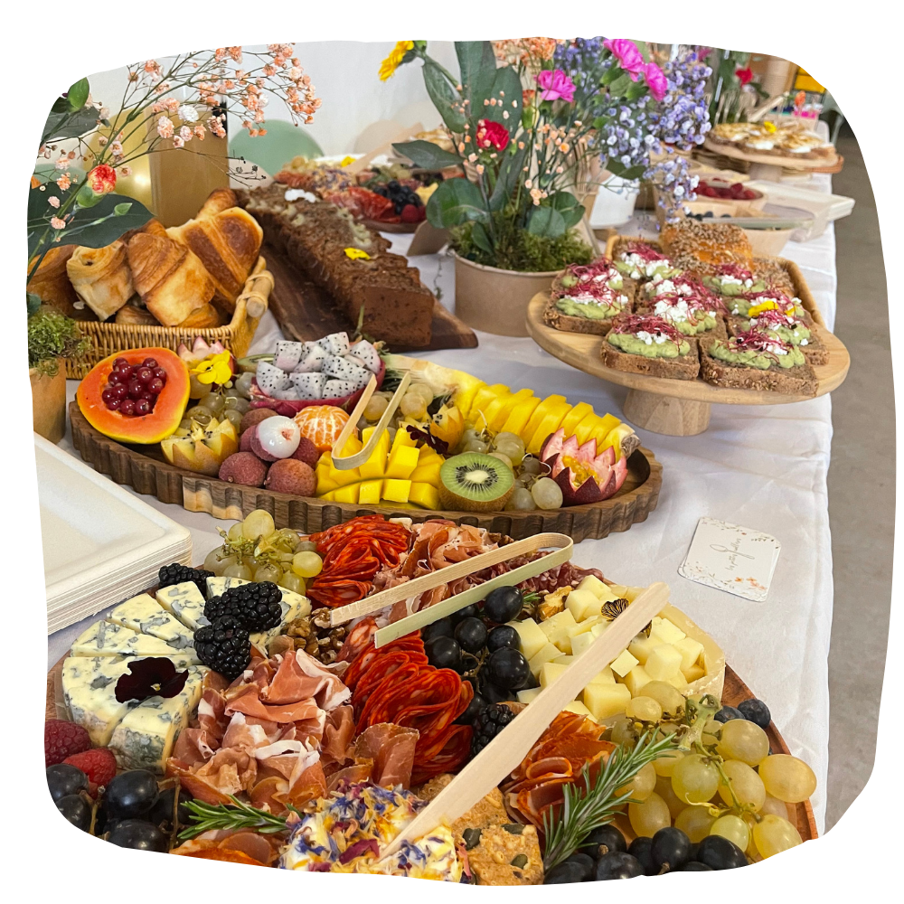 Un buffet copieux proposant des plateaux de fromages artisanaux, de charcuterie, de fruits tropicaux et de pains assortis.