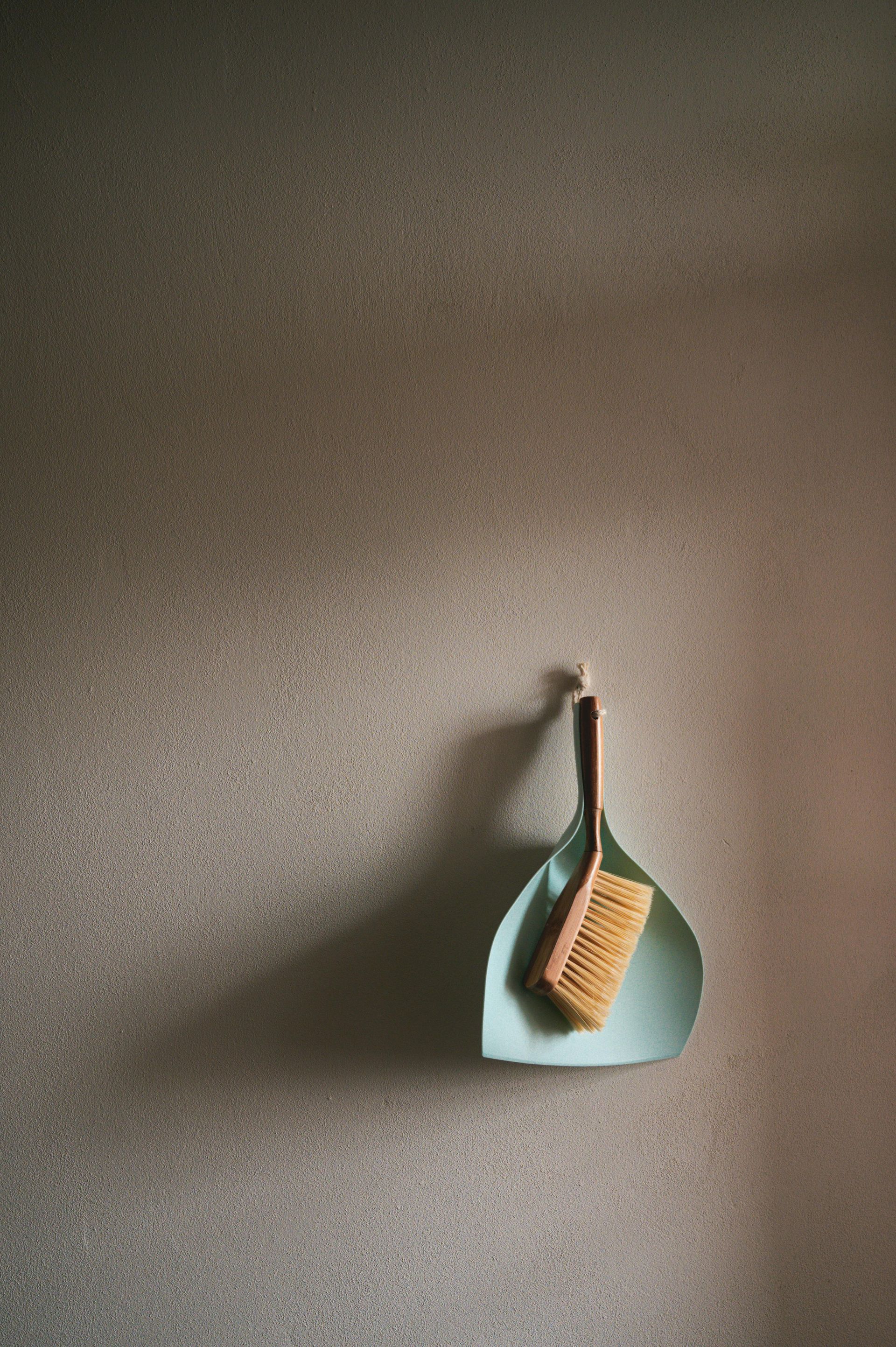 Dustpan and brush hanging on a textured, light brown wall.