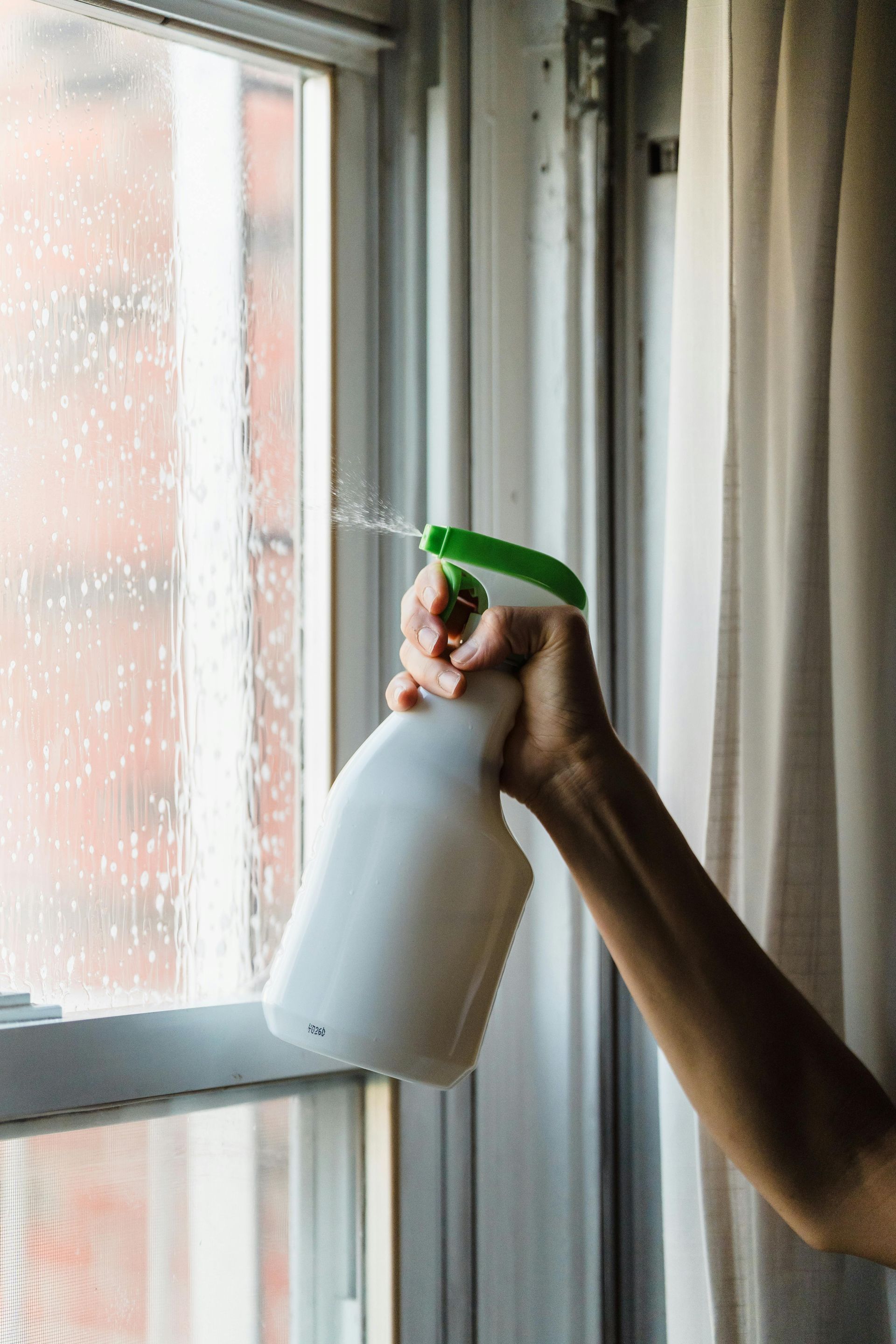 A person is spraying a window with a spray bottle.