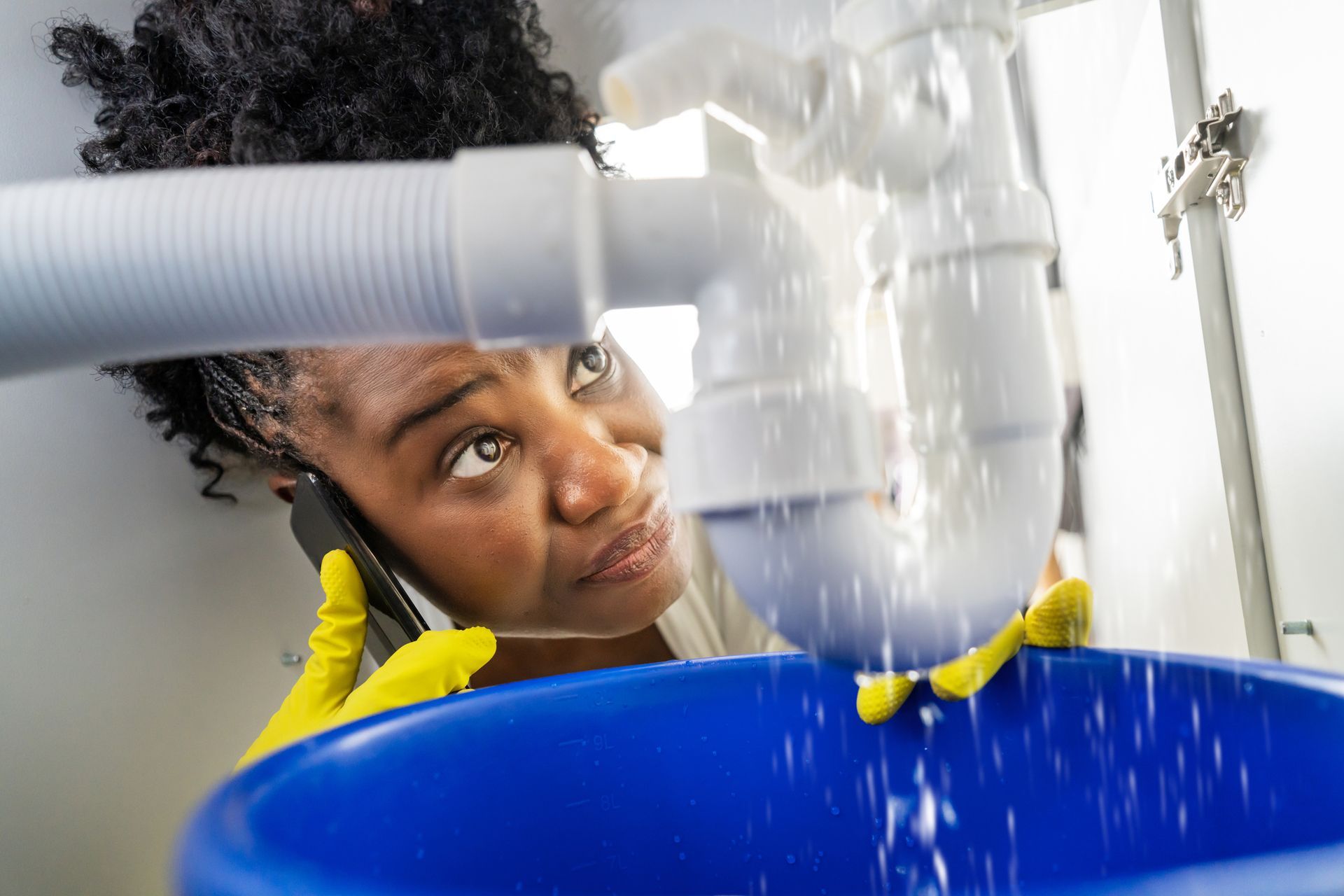 Close-up of a worried woman calling for emergency plumbing, due to a leaky sink pipe.