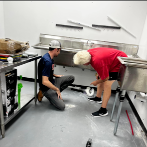 Two men fix a kitchen sink.