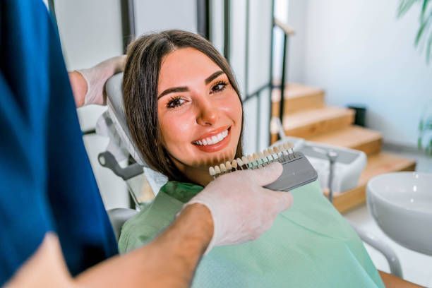 Woman in dental chair comparing teeth shades with dentist.