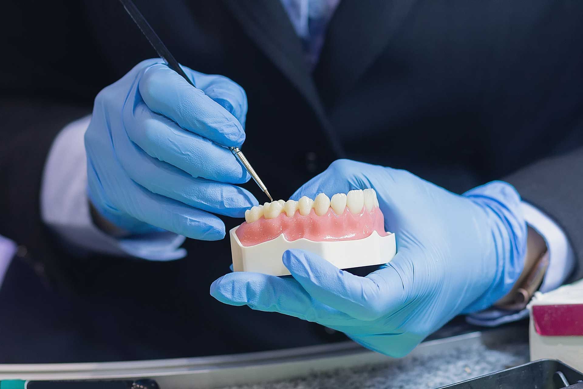 Person in blue gloves paints a dental model with a fine brush.