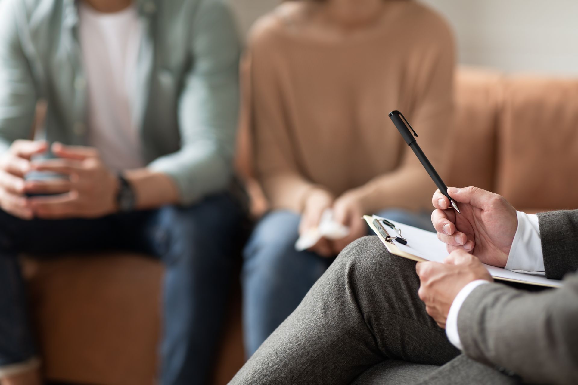 Therapist taking notes during a counseling session with two seated clients on a couch