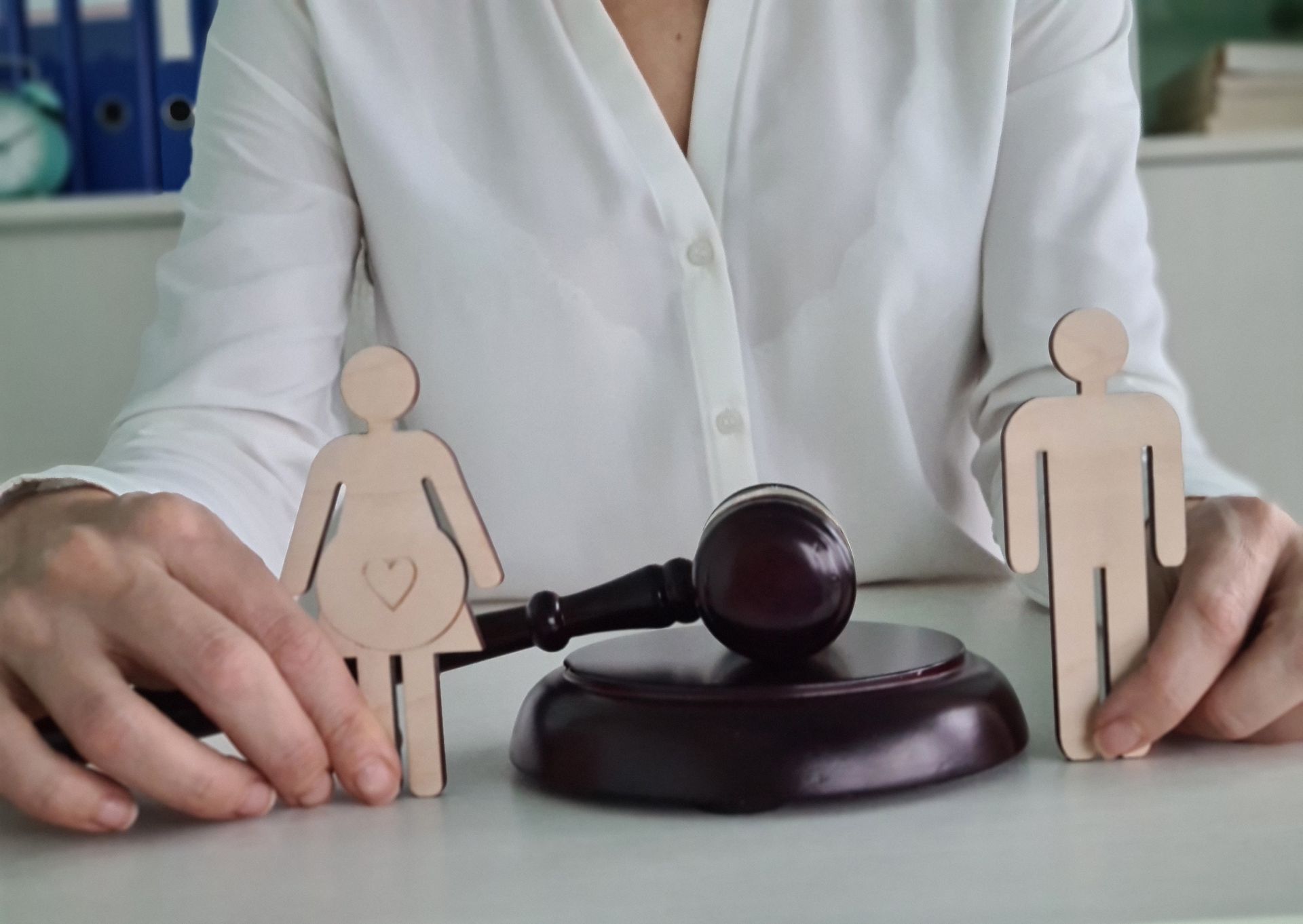 Person holds wooden male and female figures beside a judge’s gavel on a desk