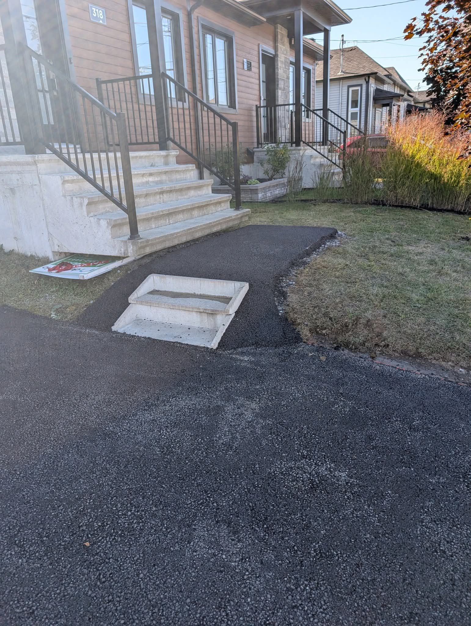 Un chemin pavé menant d'une rue asphaltée à un escalier situé à l'entrée d'une maison.
