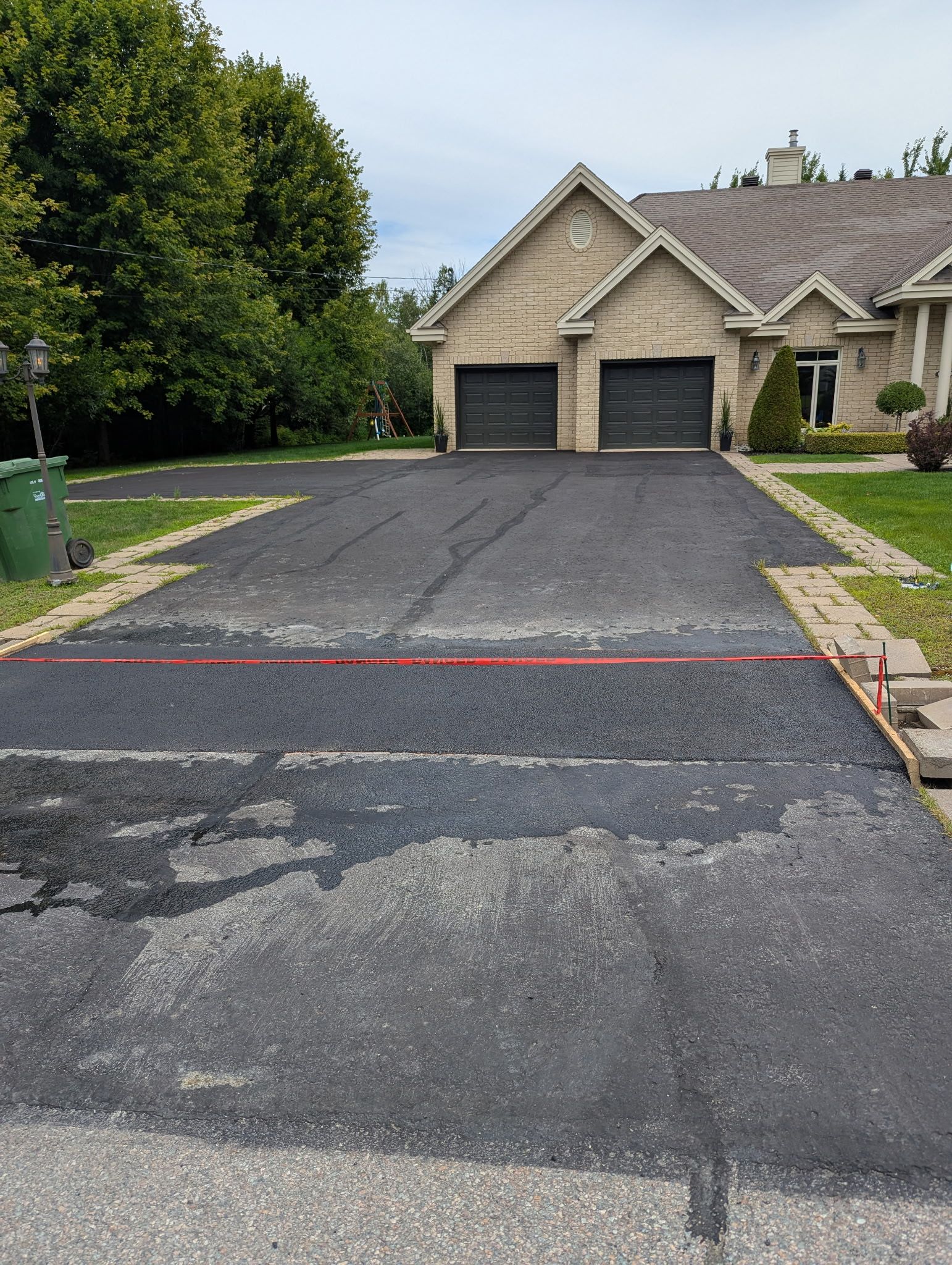 Une allée résidentielle pavée, avec un joint visible, bordée de pierres, menant à une maison avec un garage double.
