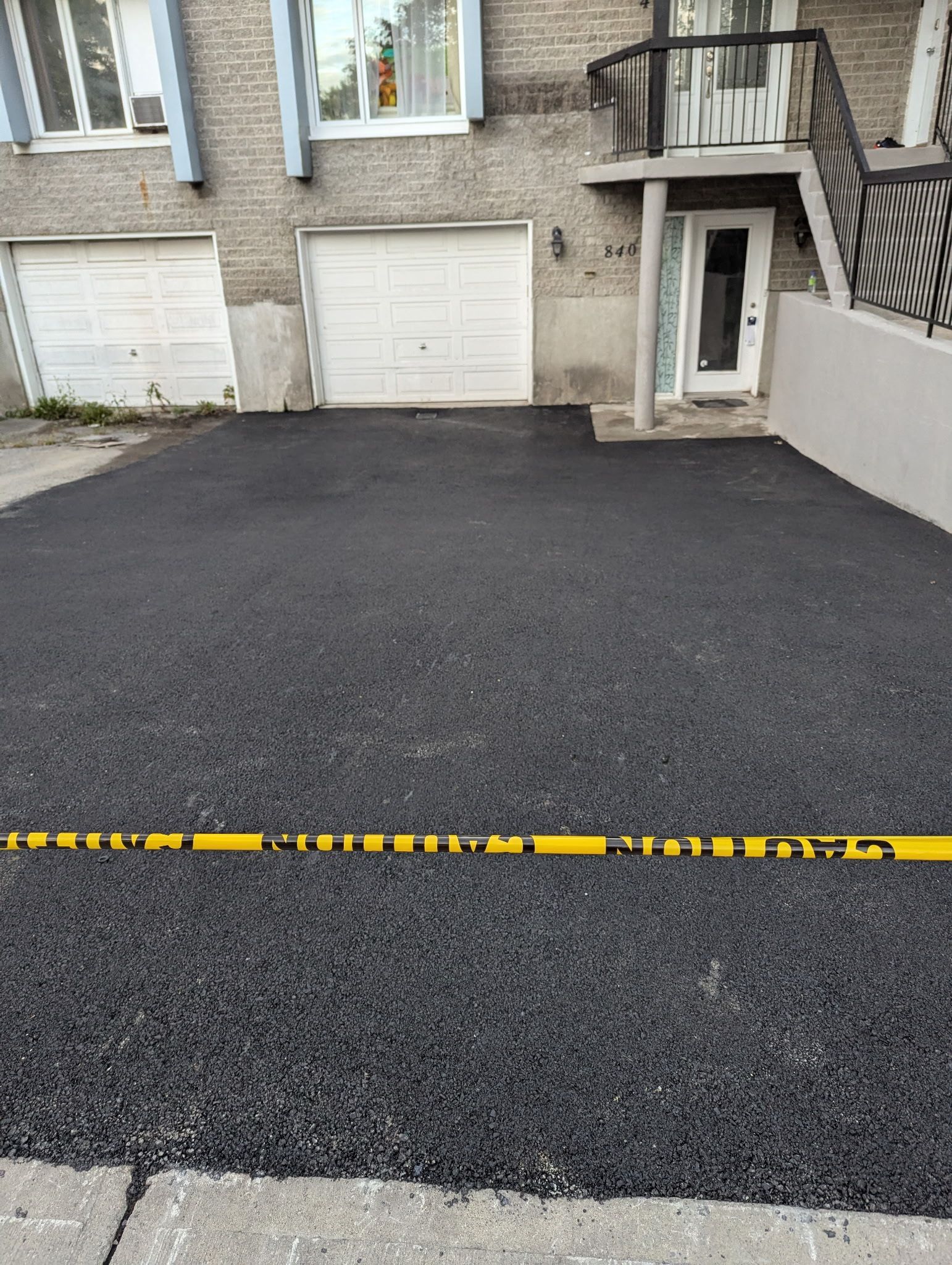 Une allée asphaltée nouvellement pavée devant une maison, bloquée par un ruban de signalisation jaune.