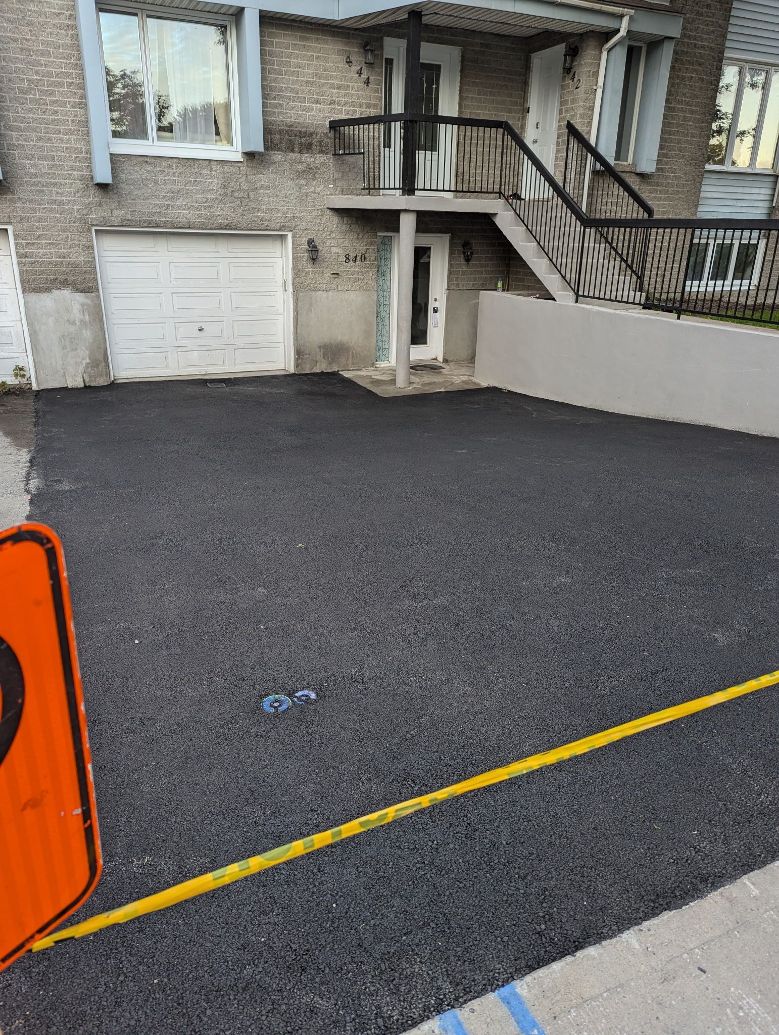 Une allée de gravier mène à une maison avec une porte de garage blanche, un escalier menant à l'étage et une ligne de délimitation jaune.