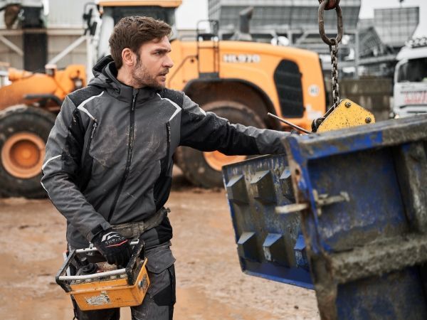 Un homme en tenue de chantier utilise une télécommande à proximité d'engins de chantier et d'un bloc de béton.