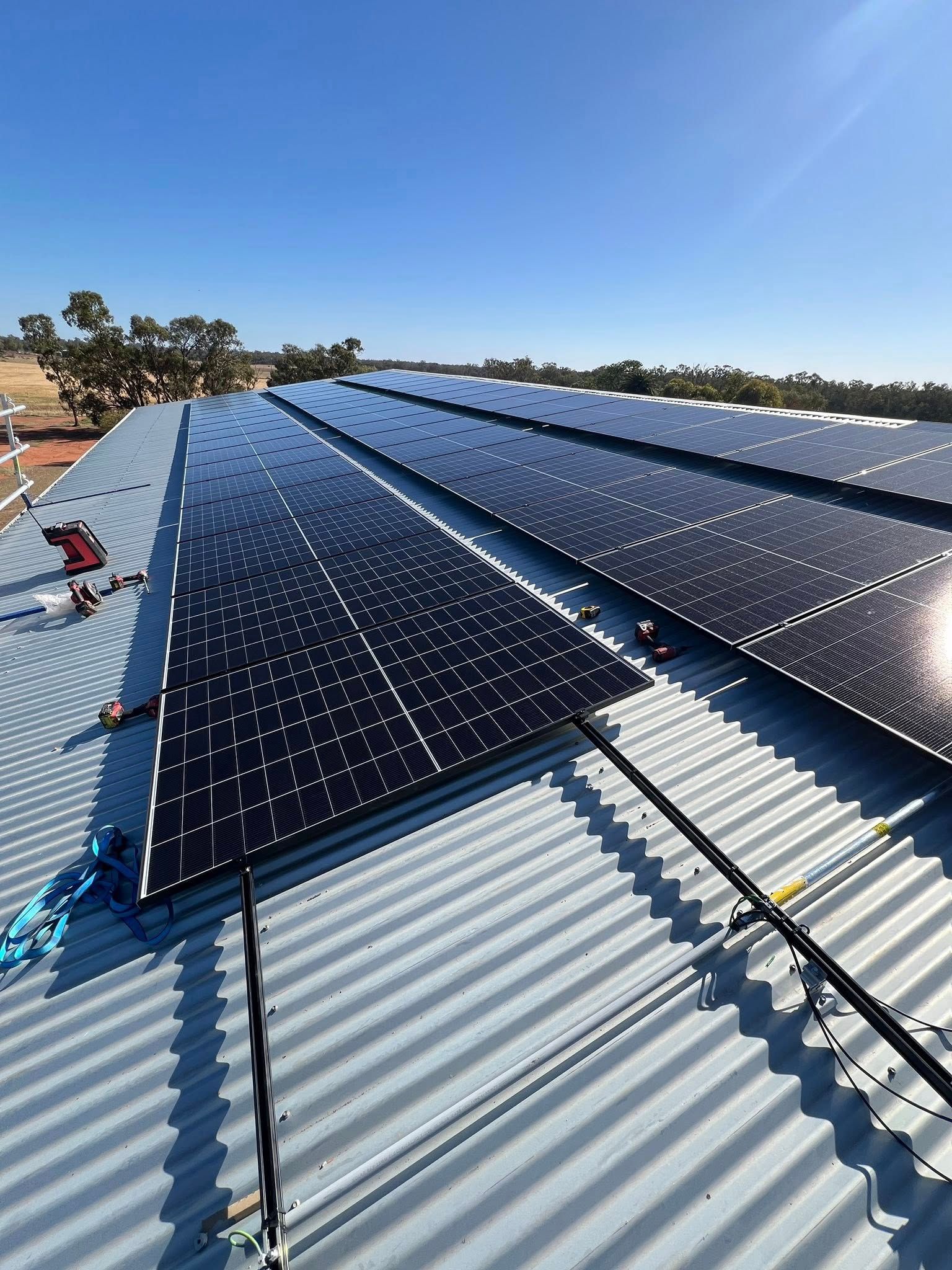 Solar Panels Installed on a Corrugated Metal Roof Under a Clear Blue Sky — Des Mullins Electrical & Solar in Wagga Wagga, NSW