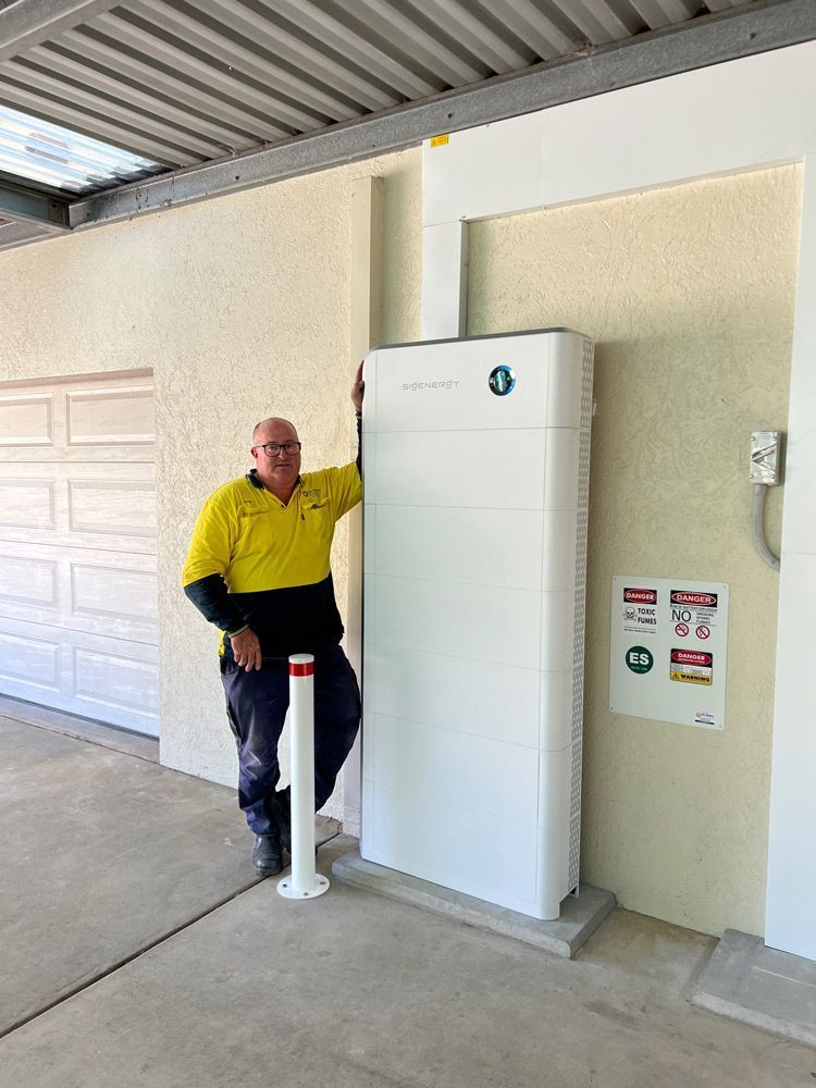 Man in Work Clothes Standing Next to a Large White Energy Storage — Des Mullins Electrical & Solar in Wagga Wagga, NSW