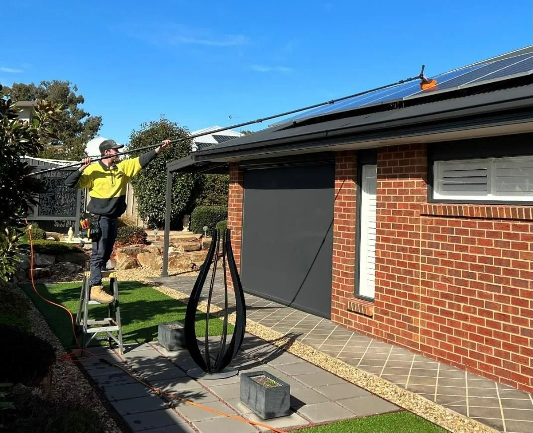 A Man Is Standing On A Ladder Solar Cleaning — Des Mullins Electrical & Solar In Wagga Wagga, NSW