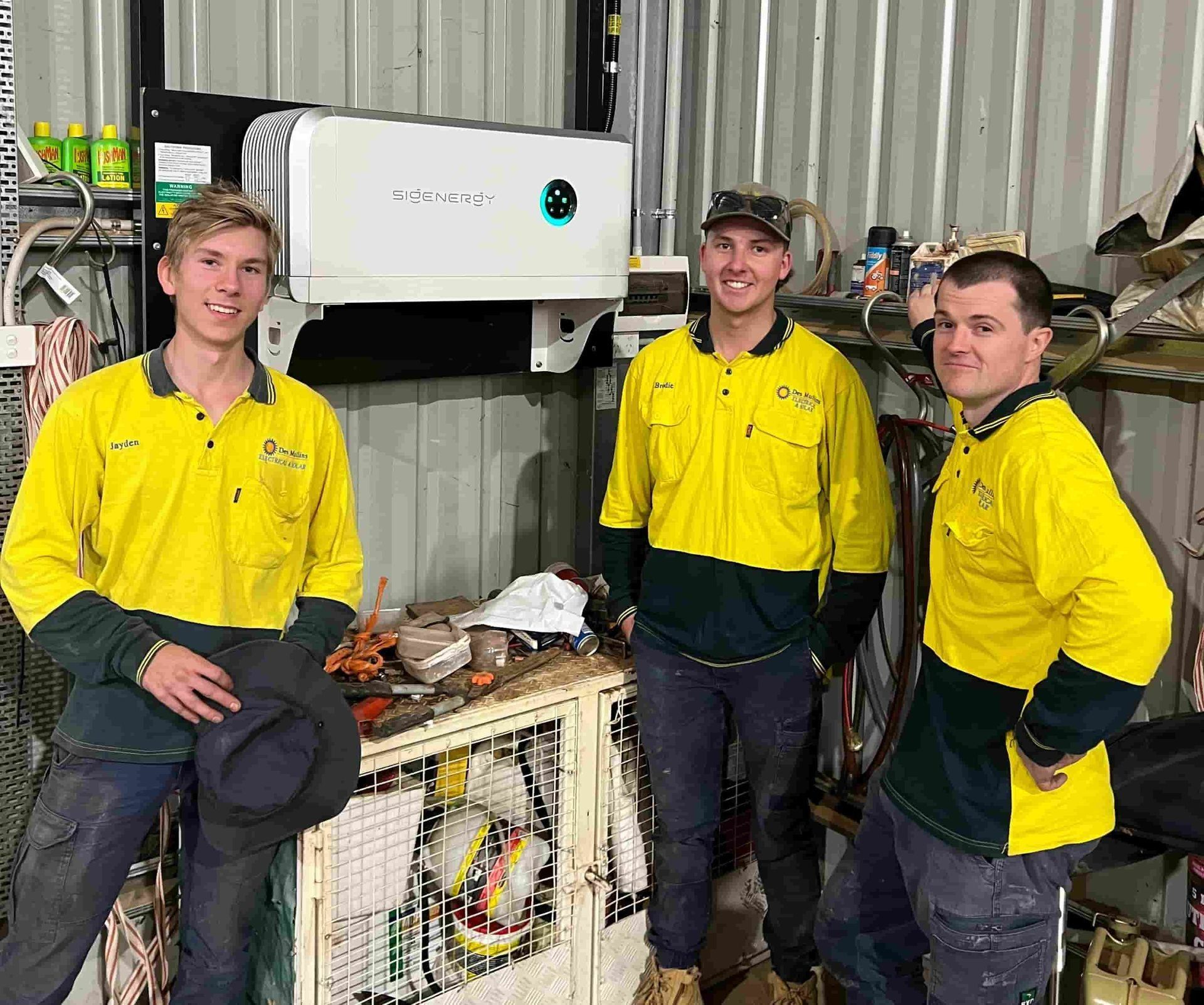 Three Workers in Yellow Shirts Stand in a Workshop — Des Mullins Electrical & Solar in Wagga Wagga, NSW