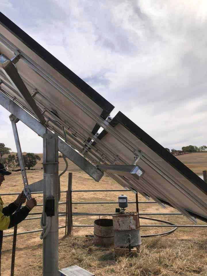 Man Adjusts Solar Panel Tilt in a Rural Field Setting — Des Mullins Electrical & Solar in Wagga Wagga, NSW