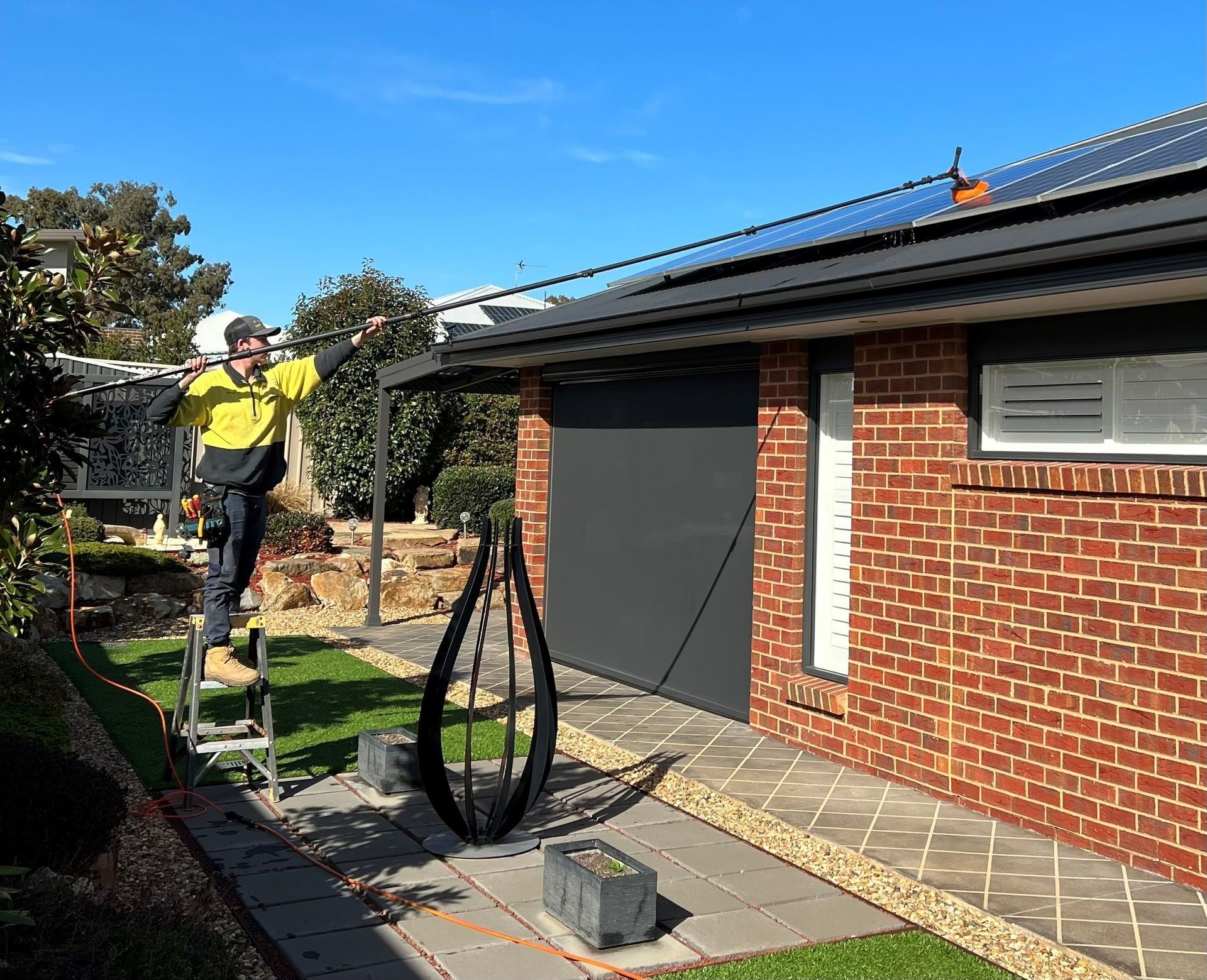 Man on Ladder Cleans Gutters of a Brick House — Des Mullins Electrical & Solar in Wagga Wagga, NSW
