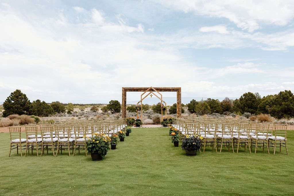Outdoor wedding ceremony setup with rows of white chairs leading to a wooden arch on a grassy lawn
