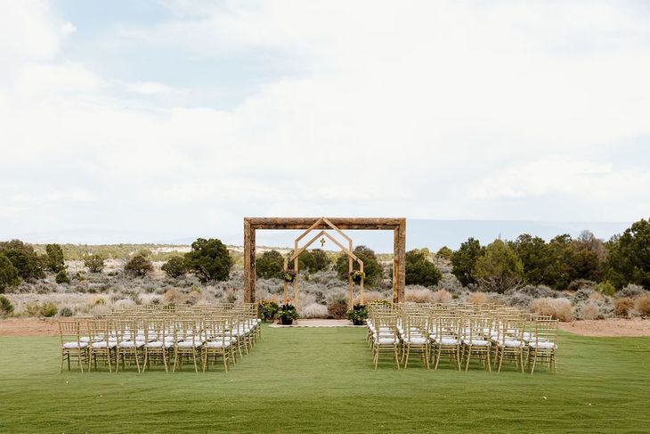 Outdoor wedding setup with wooden arch and rows of chairs on a grassy field