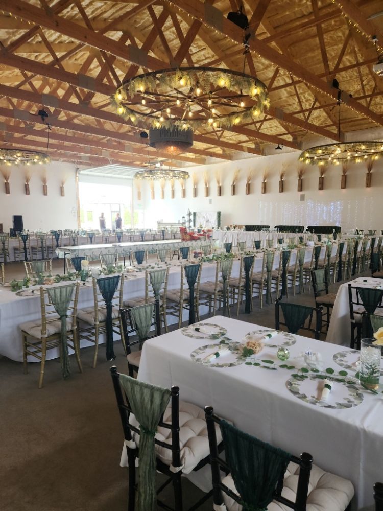 Decorated banquet hall with long tables, green chairs, white linens, and a wood truss ceiling with chandeliers