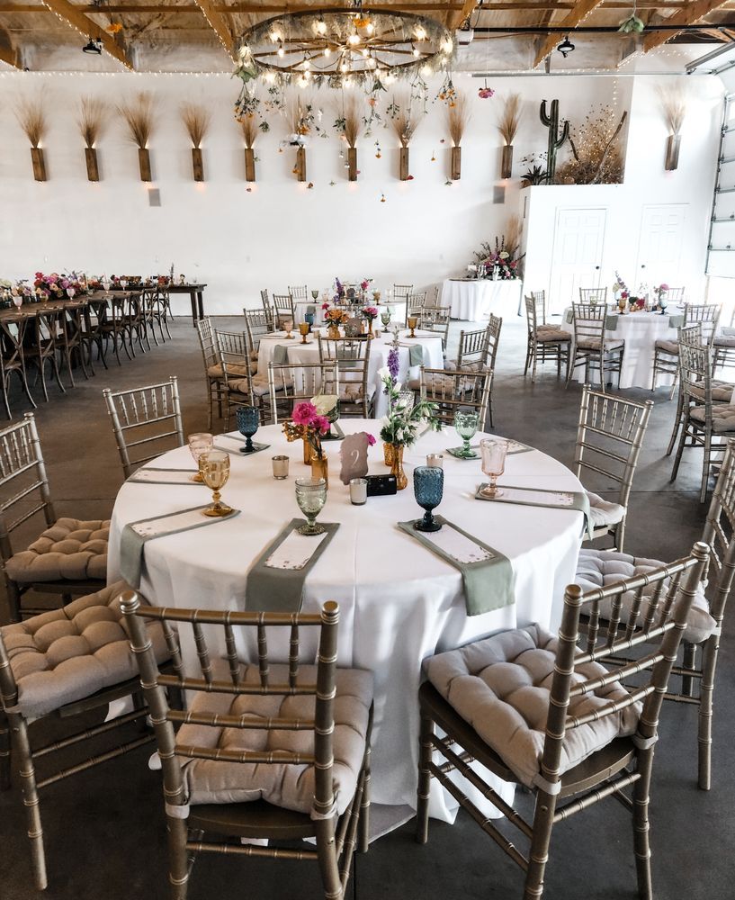 Elegant banquet hall with round tables, silver chairs, chandeliers, and floral centerpieces