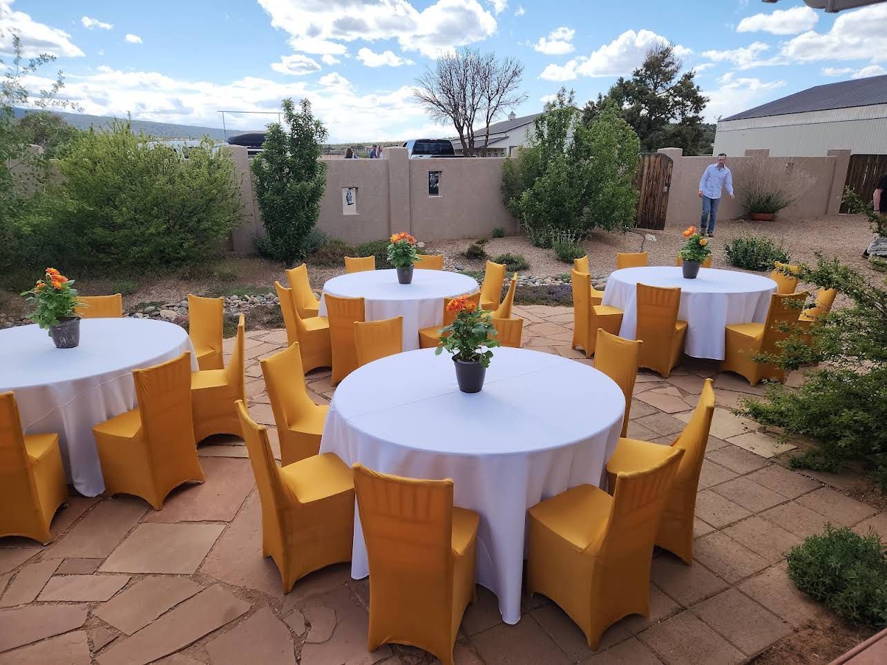 Outdoor patio with round tables and yellow chair covers set for an event in a garden courtyard.