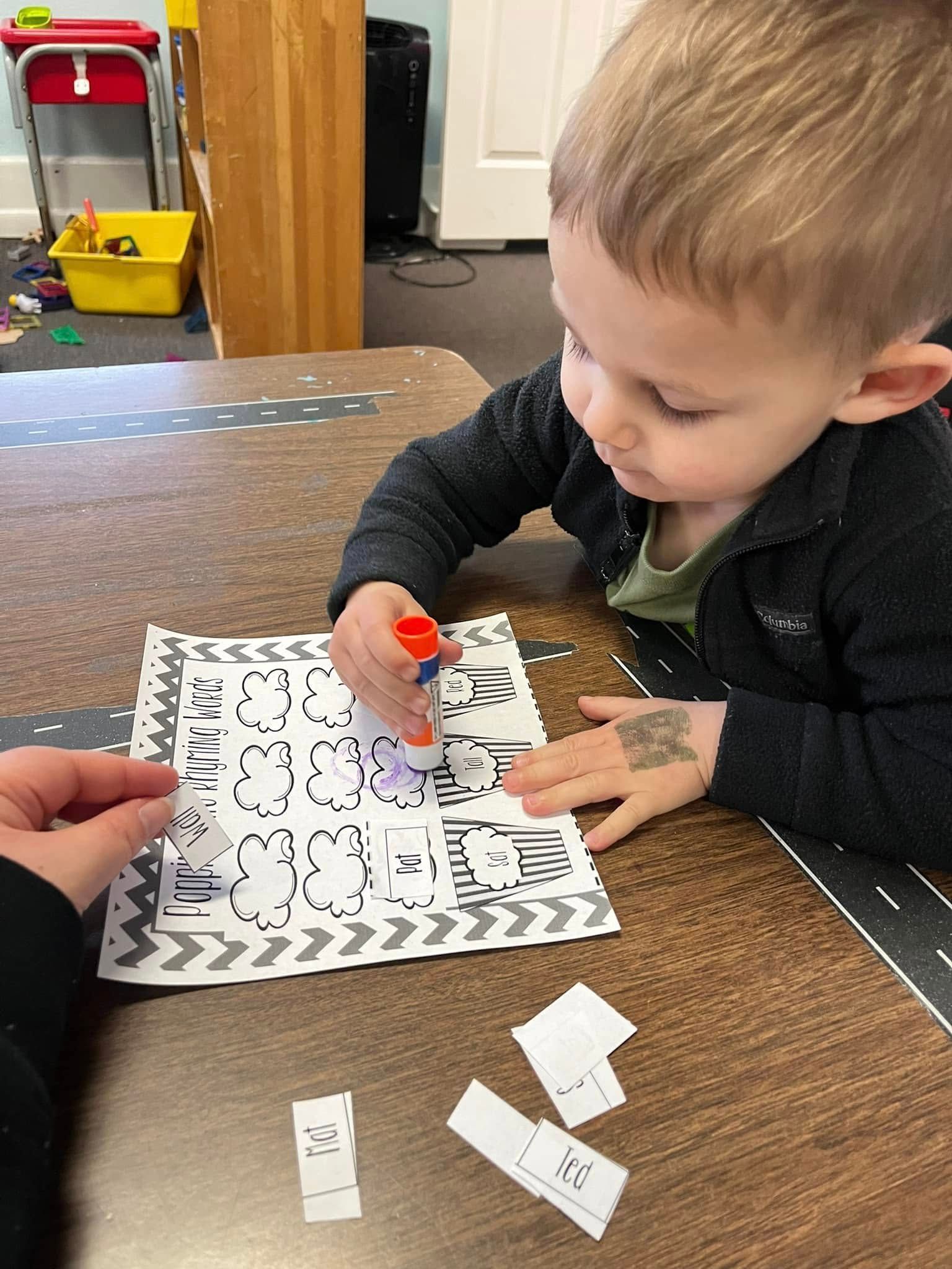 A young boy is sitting at a table cutting a piece of paper with scissors.