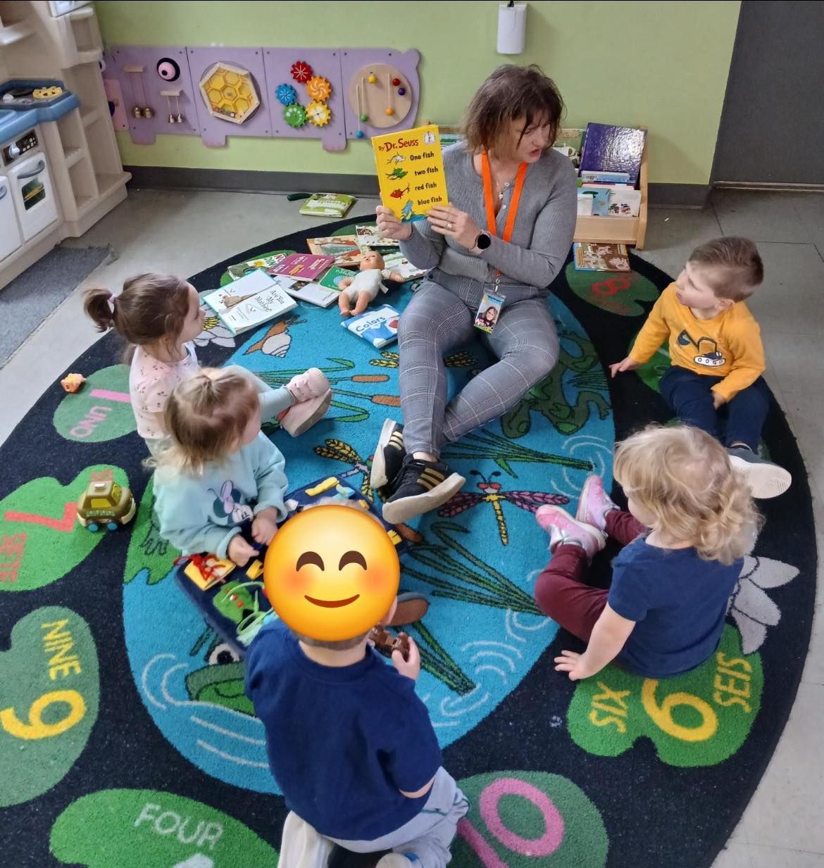 A group of children are sitting on a rug with the number six on it