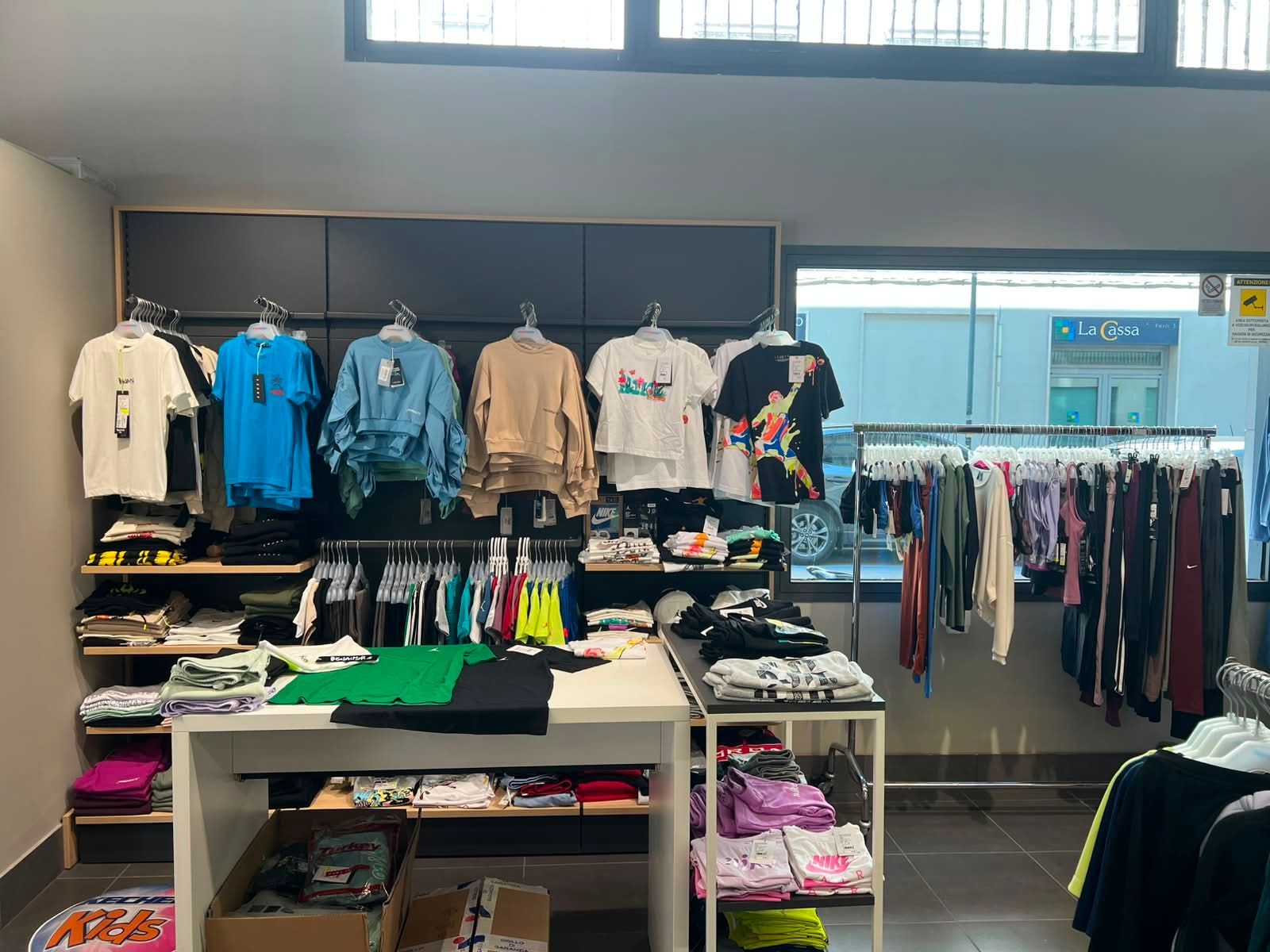 Tavolo espositivo e scaffali con abbigliamento da palestra, completi fitness coordinati e tessuti elastici per l'allenamento a Forlì.
