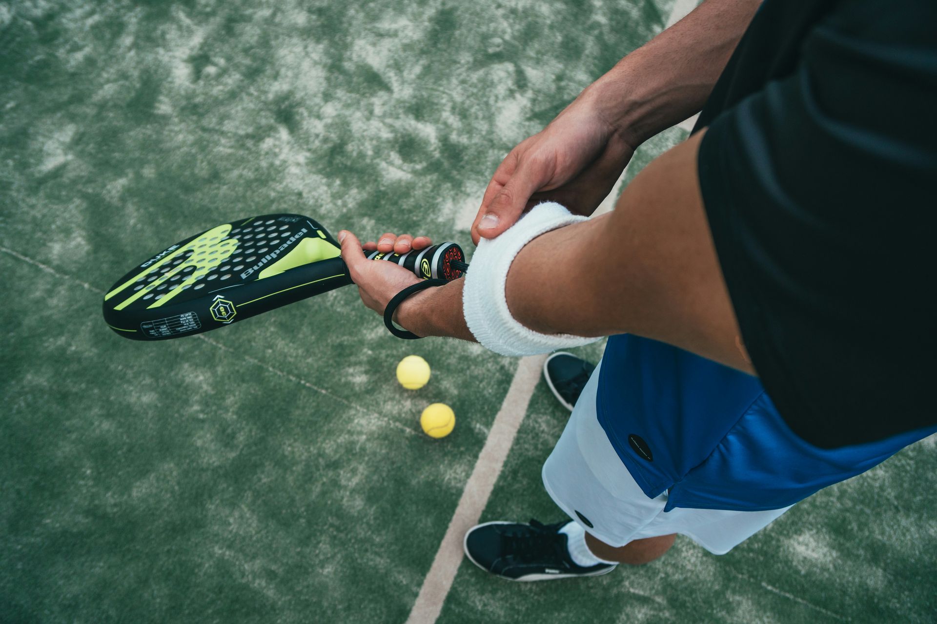 Dettaglio di un giocatore sul campo da gioco con racchetta da padel, scarpe tecniche e accessori per tennis e padel.