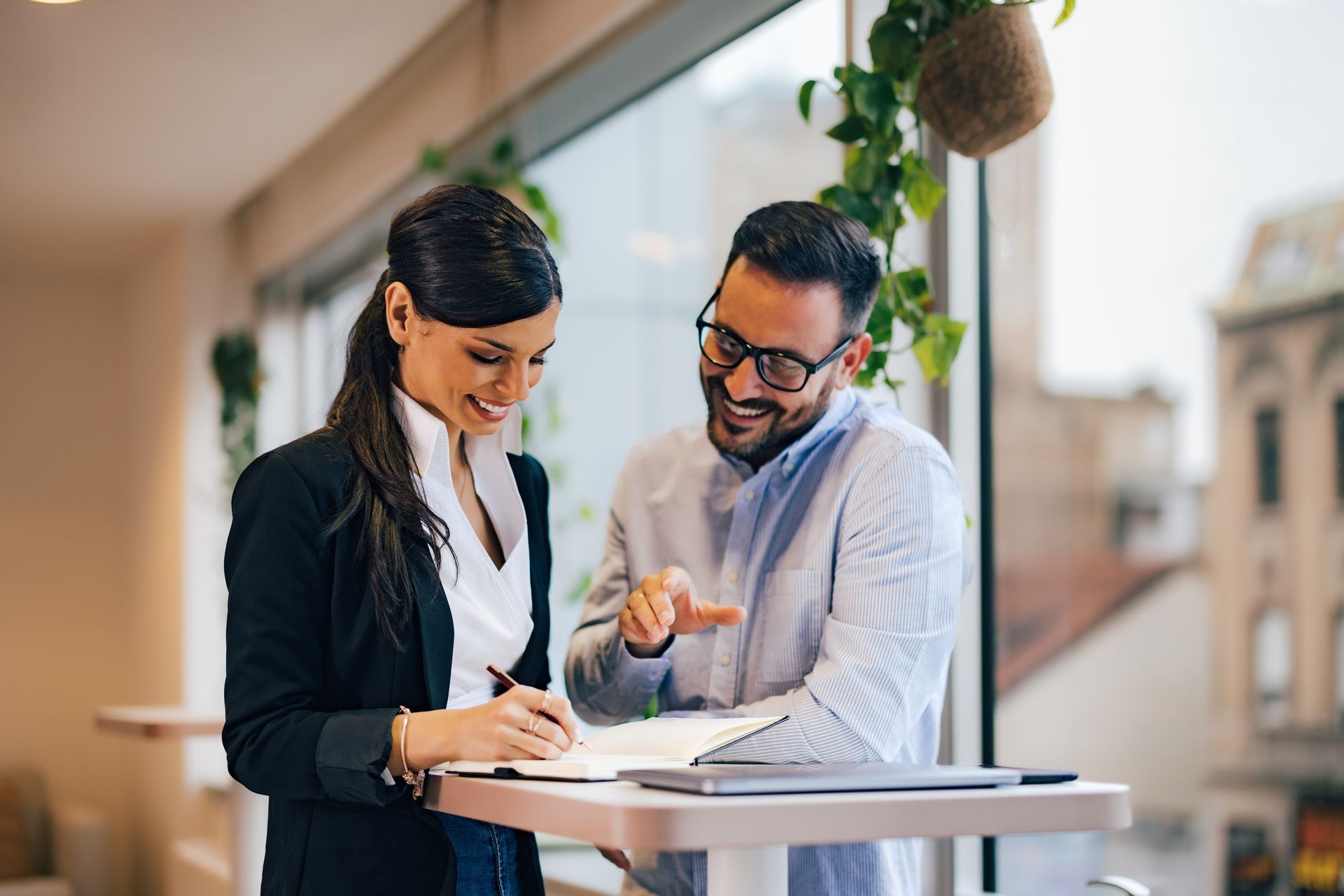 Two colleagues reviewing notes together at a standing desk in a bright office