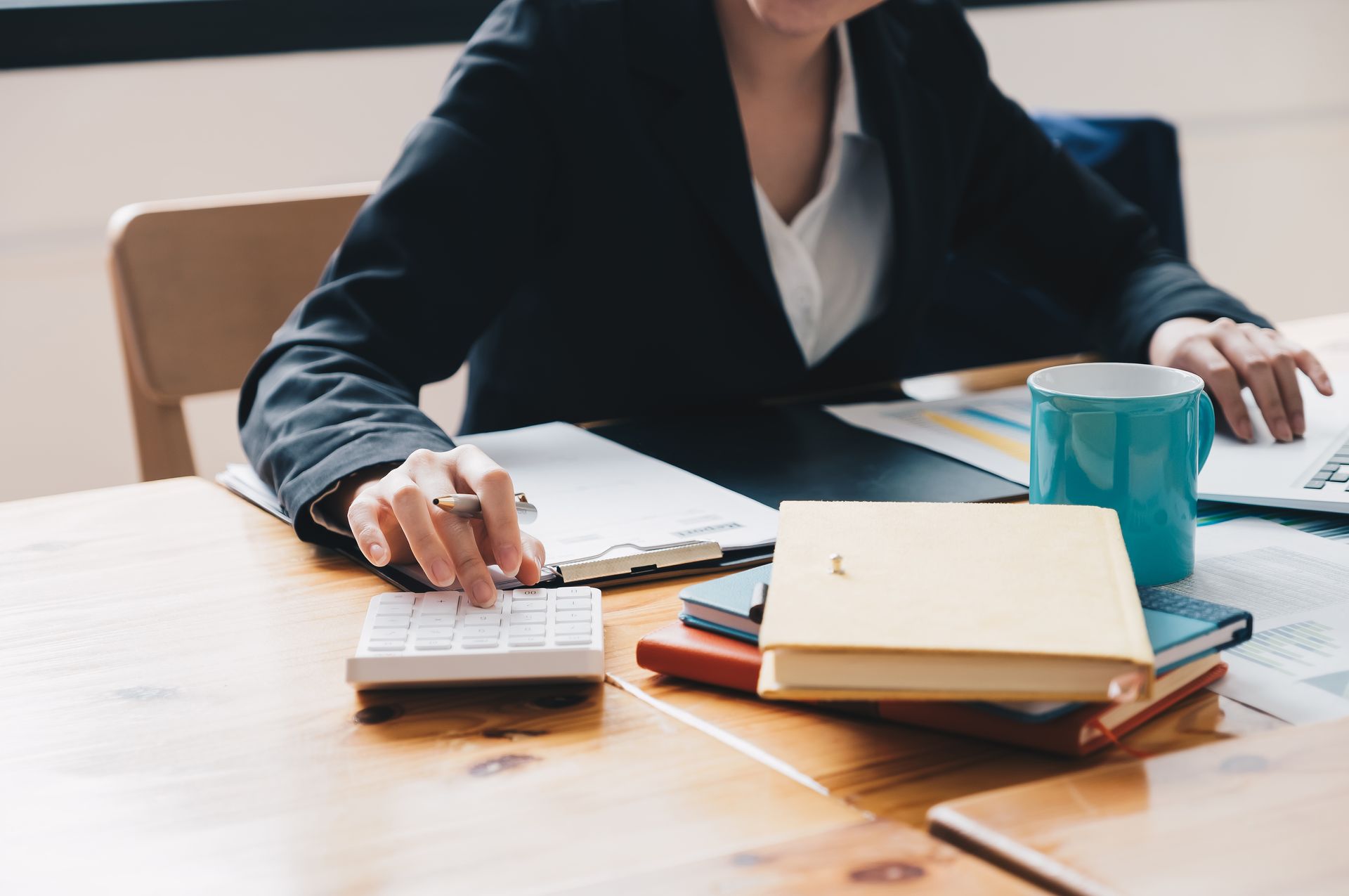 Person at a desk with notebooks, calculator, and blue mug in a bright office