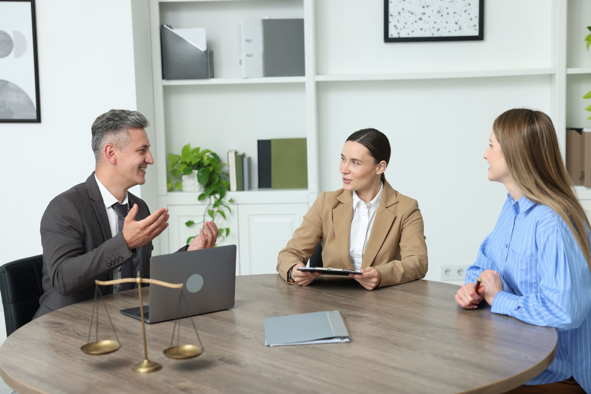 Three people in a meeting room discussing around a conference table with laptop and documents.