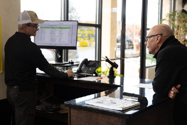 Two men are sitting at a desk in front of a computer.