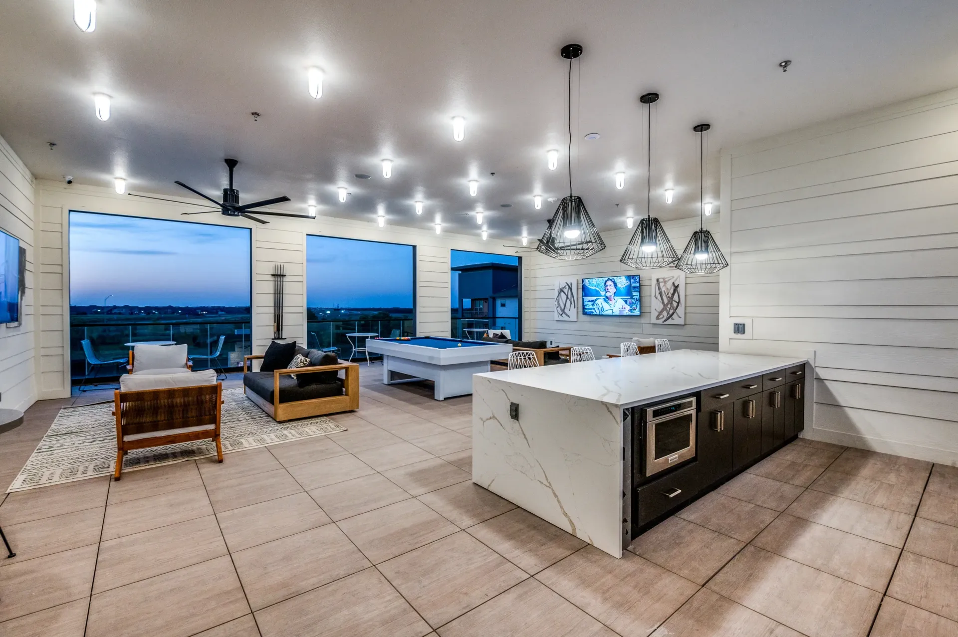 Community lounge area with pool table, seating, and kitchen island at dusk.