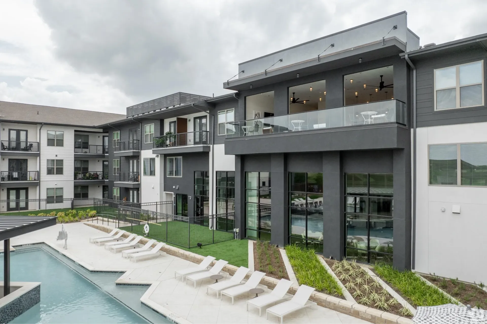 Modern apartment complex exterior with a swimming pool and lounge chairs.