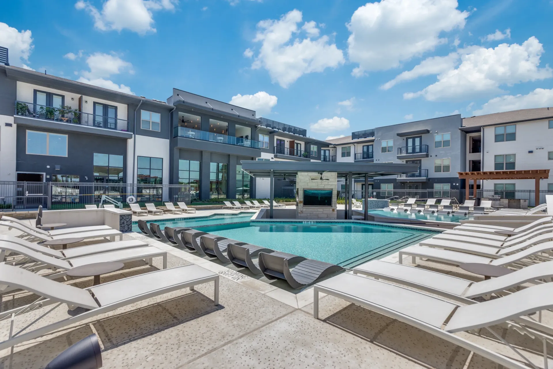 Resort-style swimming pool with lounge chairs and outdoor seating areas at a modern apartment complex.