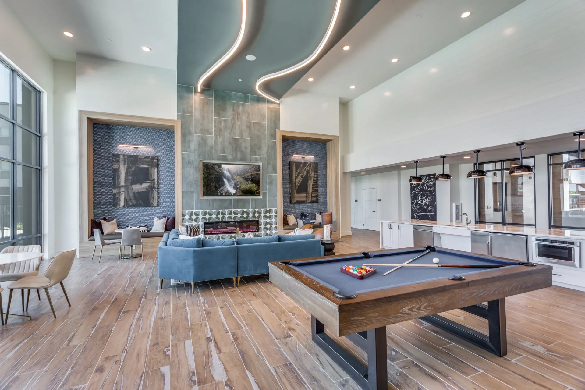 A modern community lounge with a pool table, fireplace, comfortable seating, and a bar area.