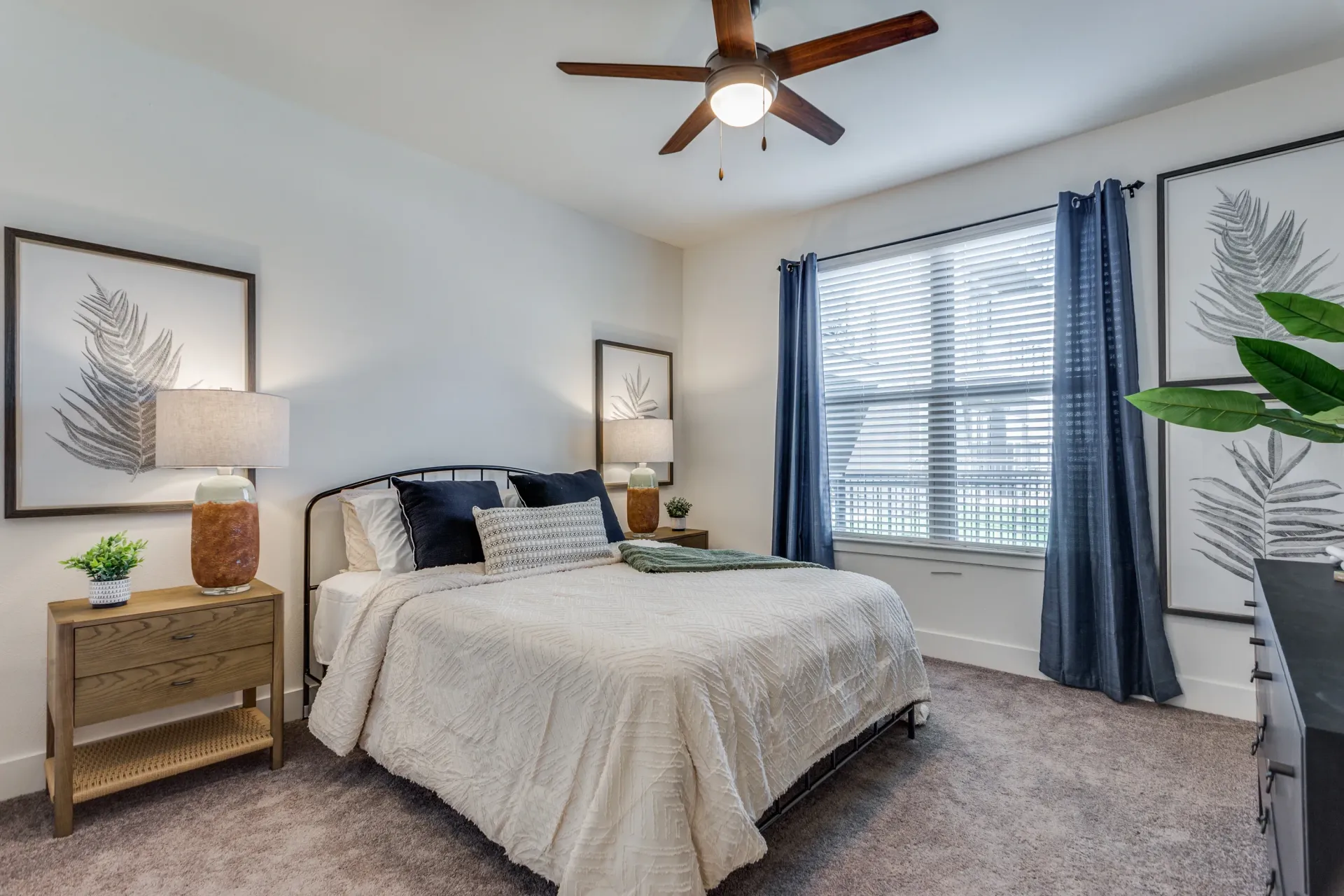 Bedroom with a queen-size bed, nightstand, ceiling fan, and large window with blue curtains.