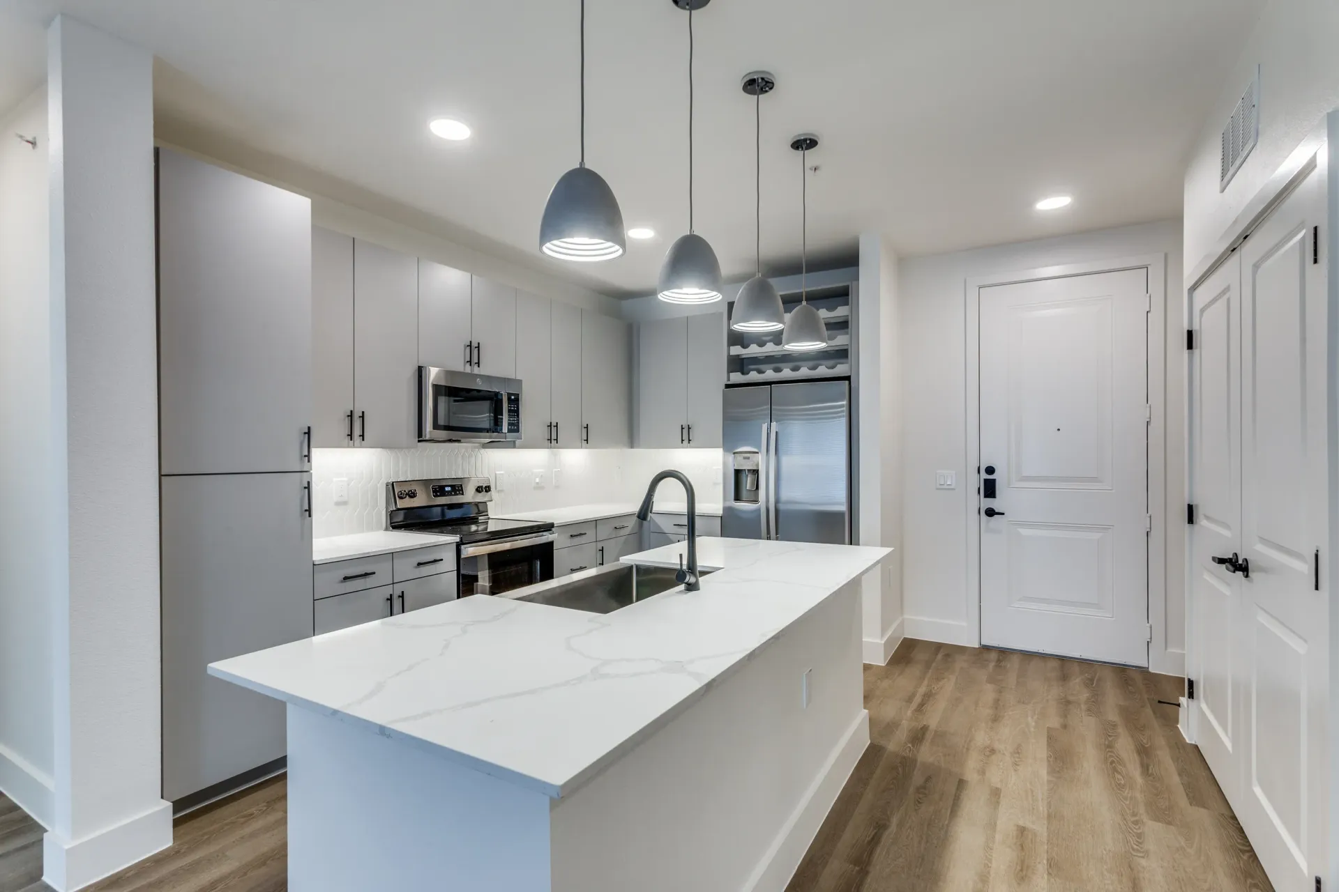 Modern apartment kitchen with a large island, stainless steel appliances, and sleek gray cabinetry.
