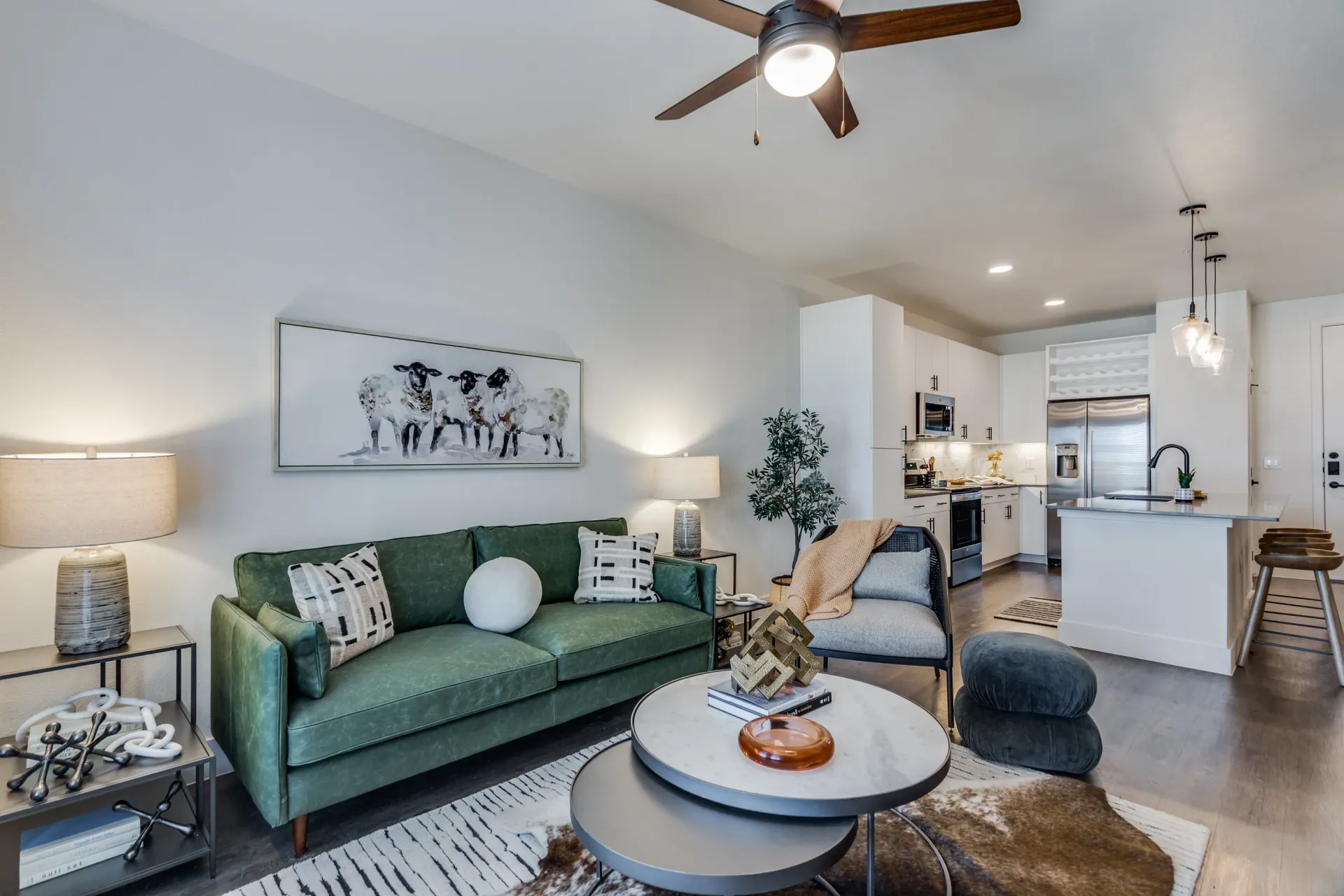 Bright living room with green sofa, round coffee table, and open kitchen in the background.