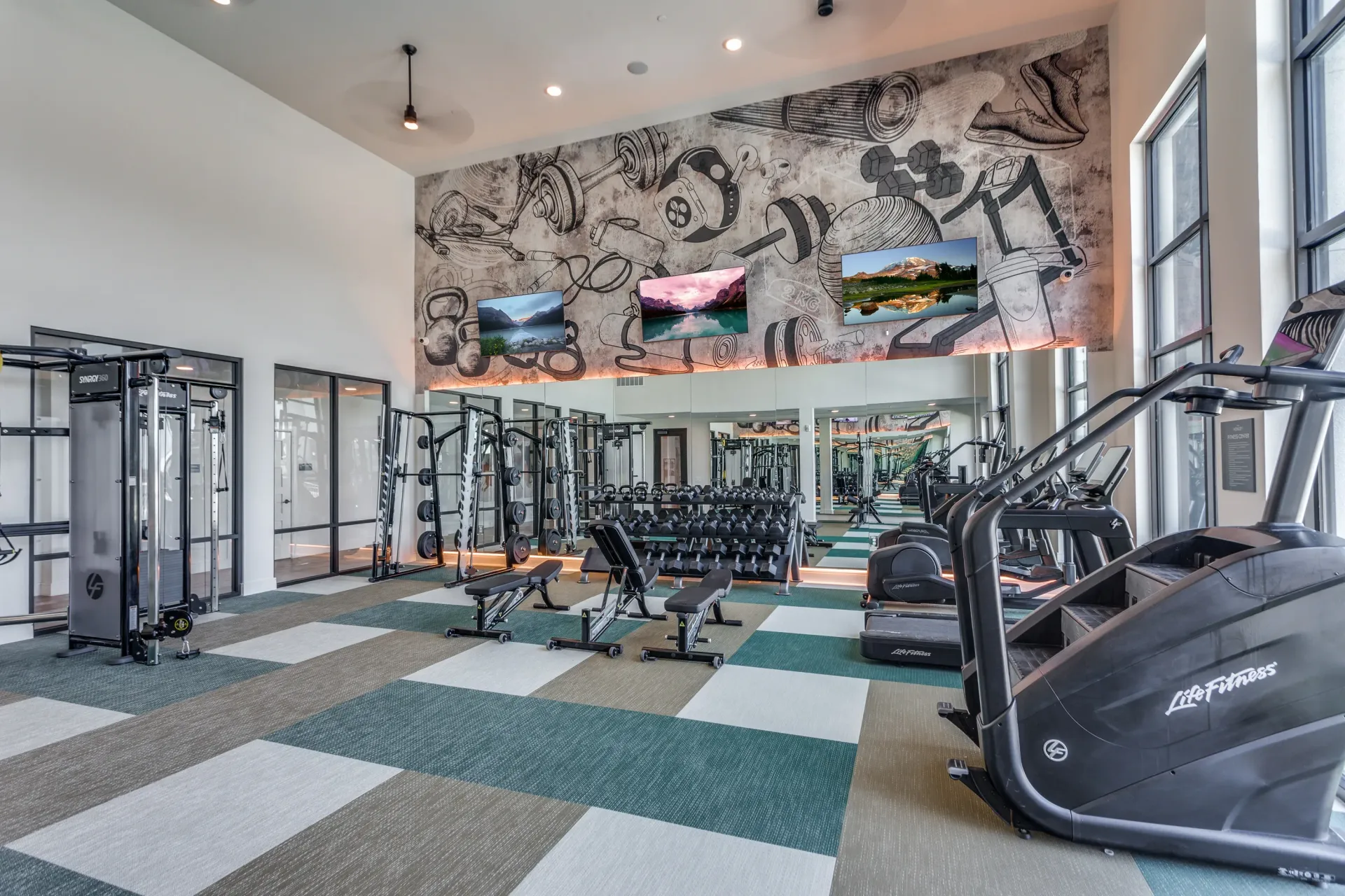 Modern gym with weight machines, free weights, cardio equipment, and a motivational mural.