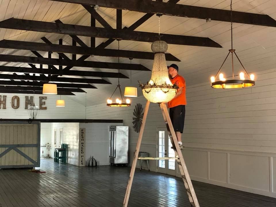 A man on a ladder hanging a chandelier in a room with a sign that says home