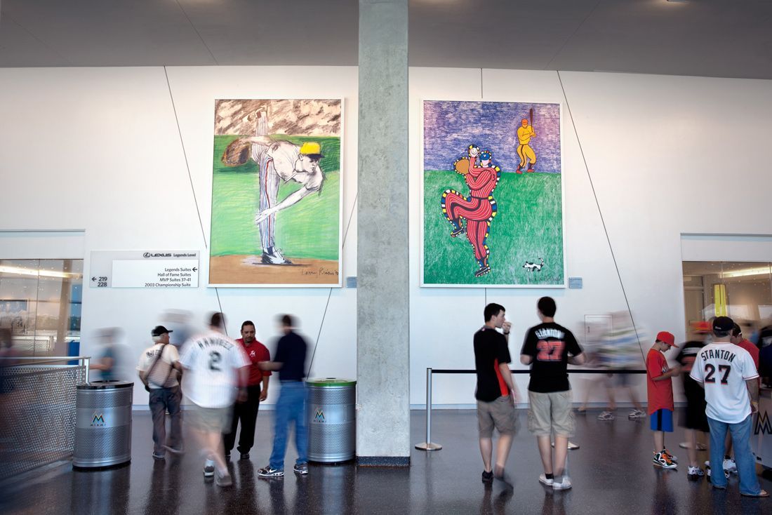 Large paintings of baseball players hang in a modern lobby. People mill about near trash cans.