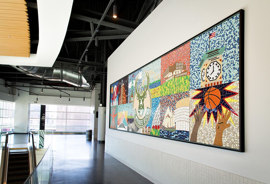 Large, colorful mosaic art hanging on a white wall in a modern gallery space with a long hallway.
