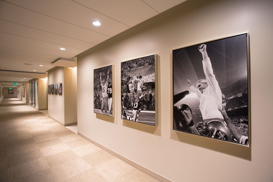 Hallway with black and white framed photos on the wall. Carpeted floor, overhead lighting.
