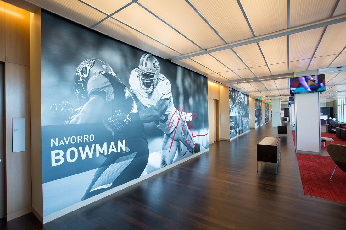 Hallway with large black and white photos of football players on the walls; wooden floor, red carpet.