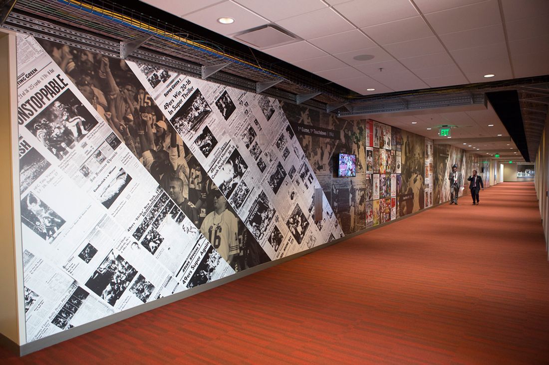 Long hallway with a wall decorated with newspaper clippings, a red carpet, and a person walking.