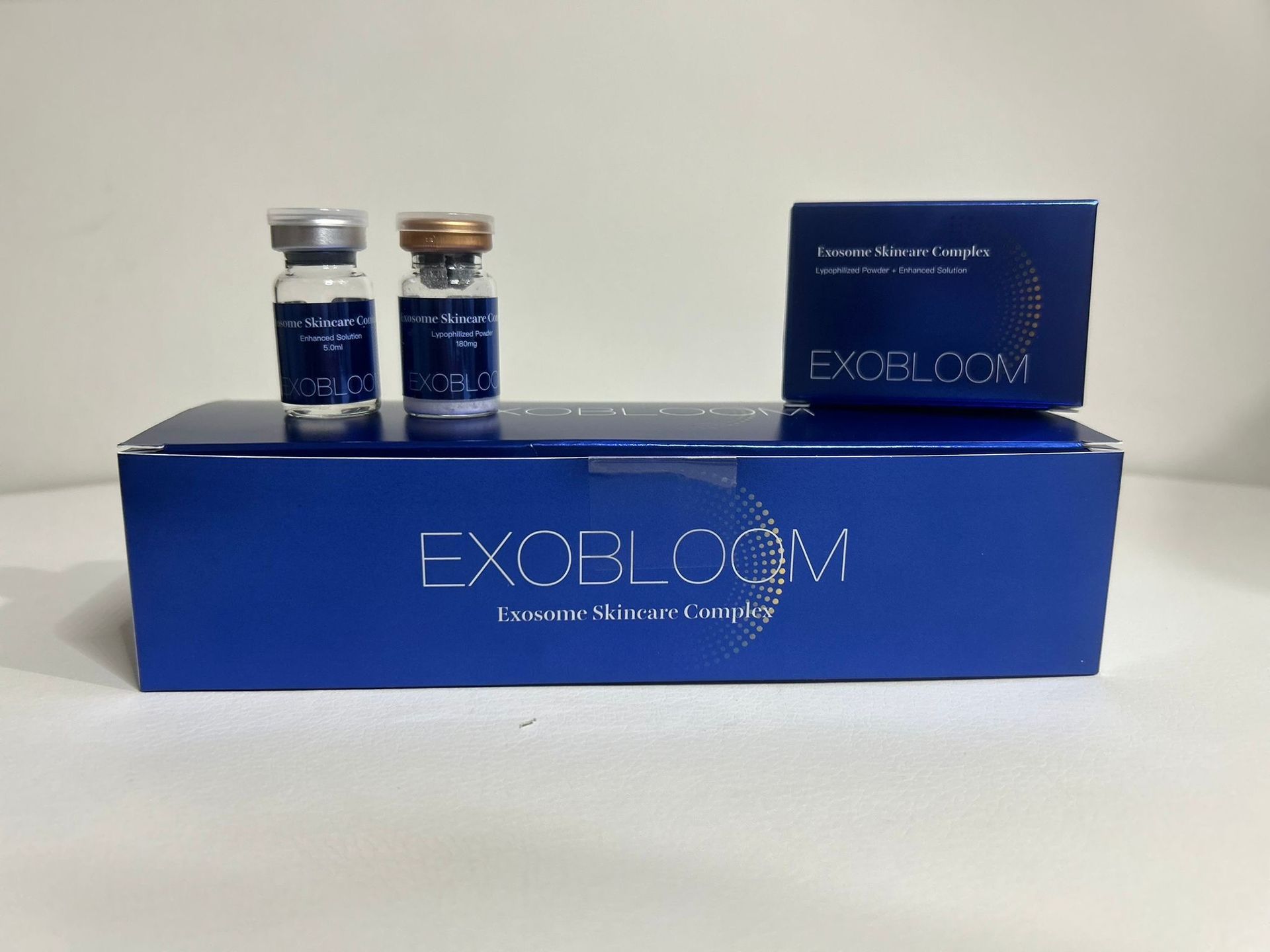 Two vials and a box of EXOBROOM skin care products, on a blue box, white background.